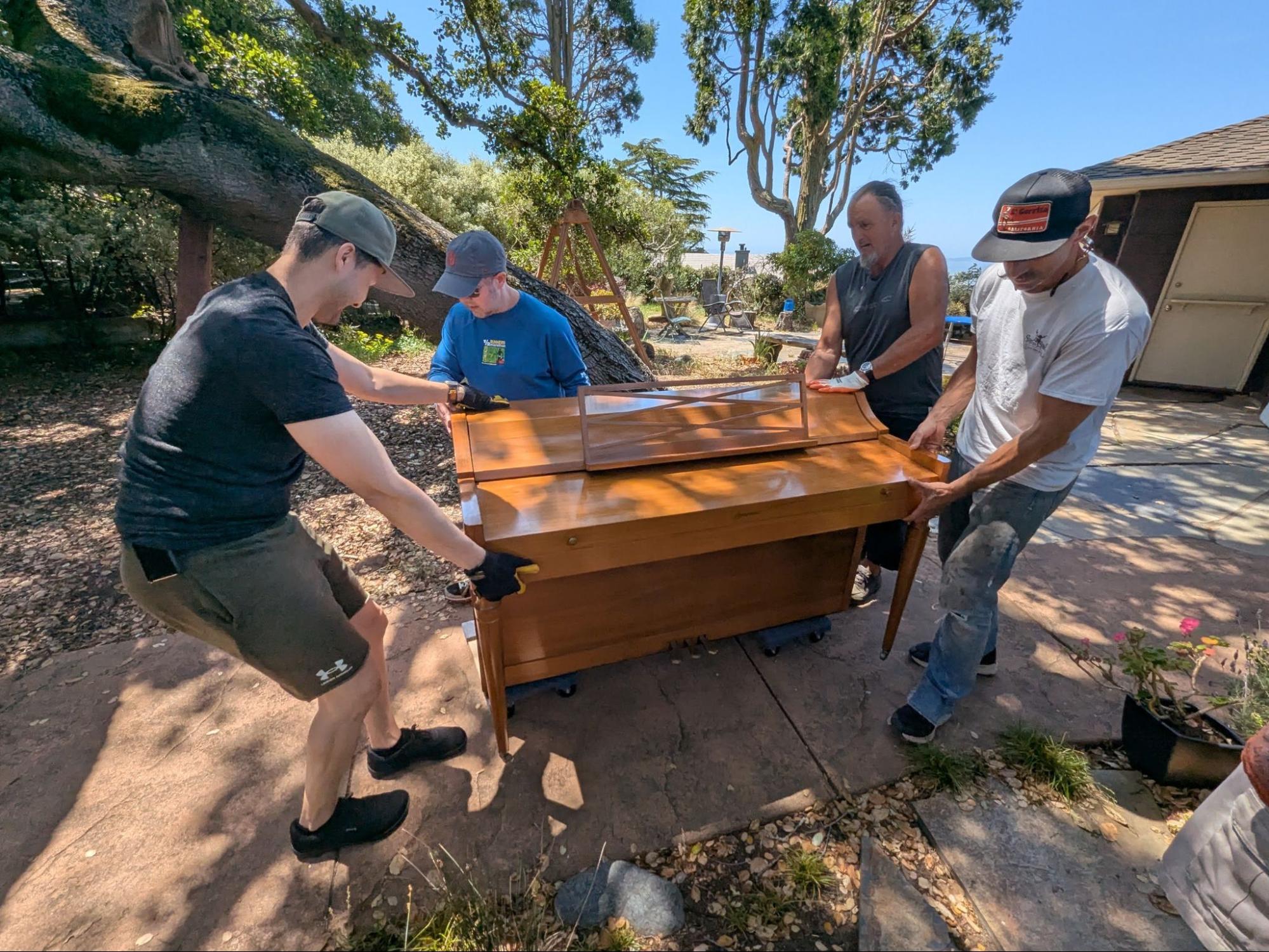 Handy Helpers volunteers moving a piano together on a sunny patio