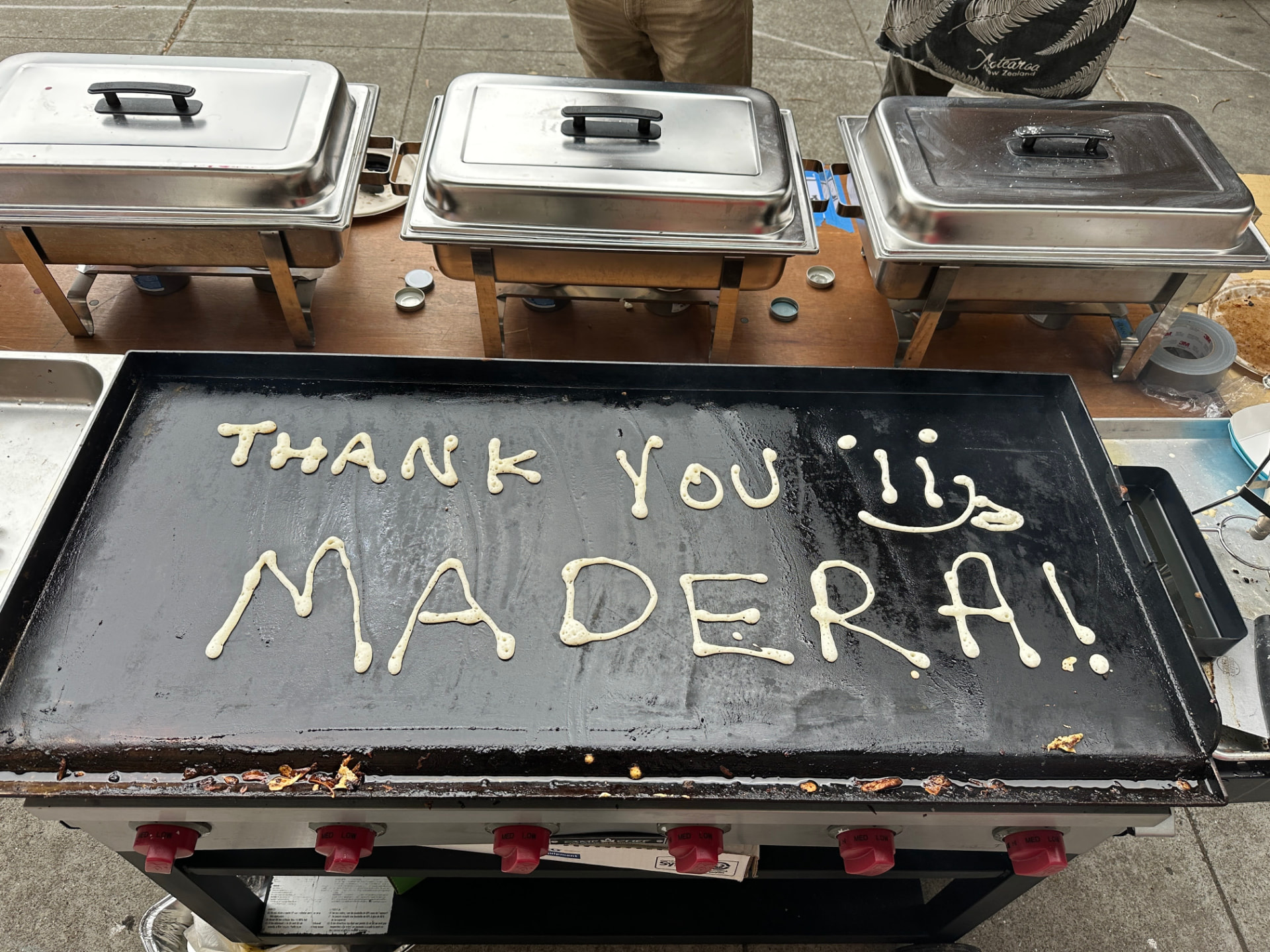 Pancake batter spelling “Thank you Madera!” with a smiley face piped onto an outdoor griddle at a school breakfast